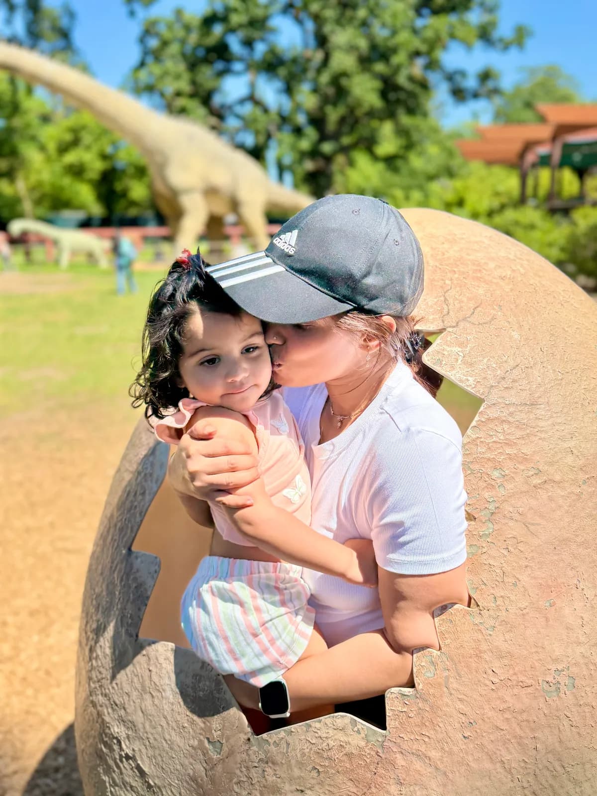 Toddler being kissed inside a giant dinosaur egg at a park