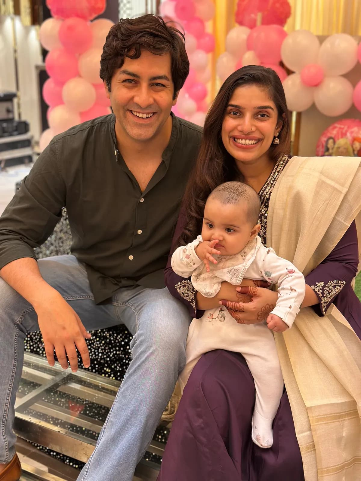 Abhay and his partner holding their baby at a family event with pink balloons